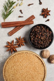 Different spices in bowls, nuts and fir branch on light gray textured table, flat lay