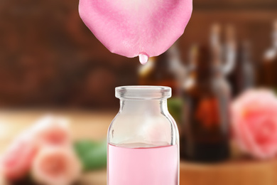 Essential oil dripping from petal into bottle against blurred background 