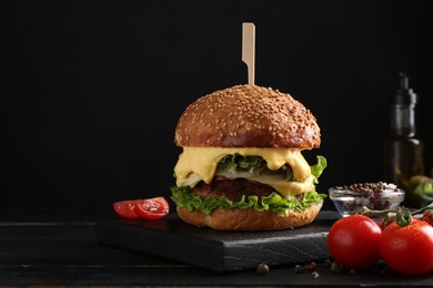 Photo of Tasty vegetarian burger, tomatoes and spices on black wooden table. Space for text