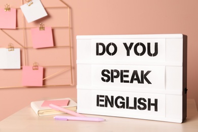 Photo of Stand with question Do You Speak English and stationery on table near pink wall