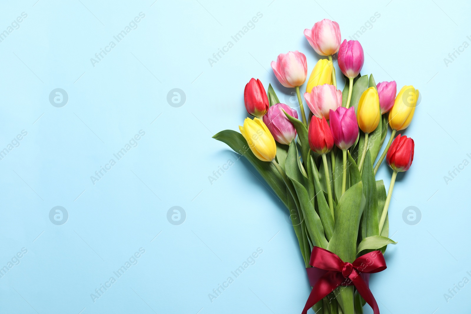Photo of Beautiful colorful tulip flowers and ribbon on light blue background, flat lay. Space for text