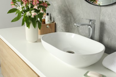 Photo of Vase with beautiful Alstroemeria flowers and toiletries near sink in bathroom