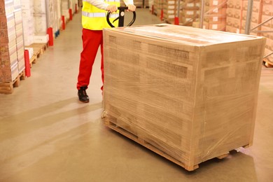 Image of Worker moving wooden pallets wrapped in stretch indoors, closeup