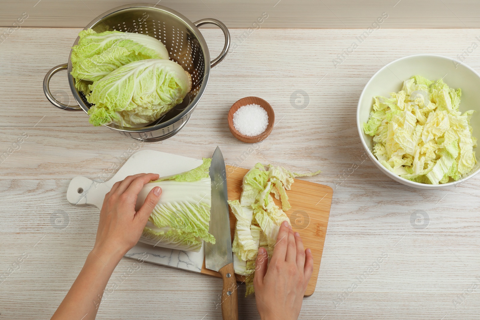 Photo of Woman cutting Chinese cabbage at white wooden kitchen table, top view