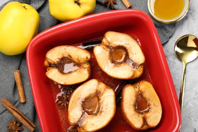 Tasty baked quinces with honey in dish on grey textured table, flat lay