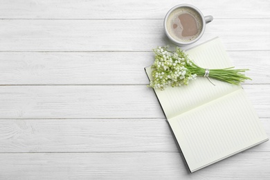 Flat lay composition with notebook, lily of the valley bouquet and coffee on white wooden background. Space for text