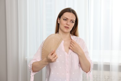 Photo of Woman waving hand fan to cool herself at home
