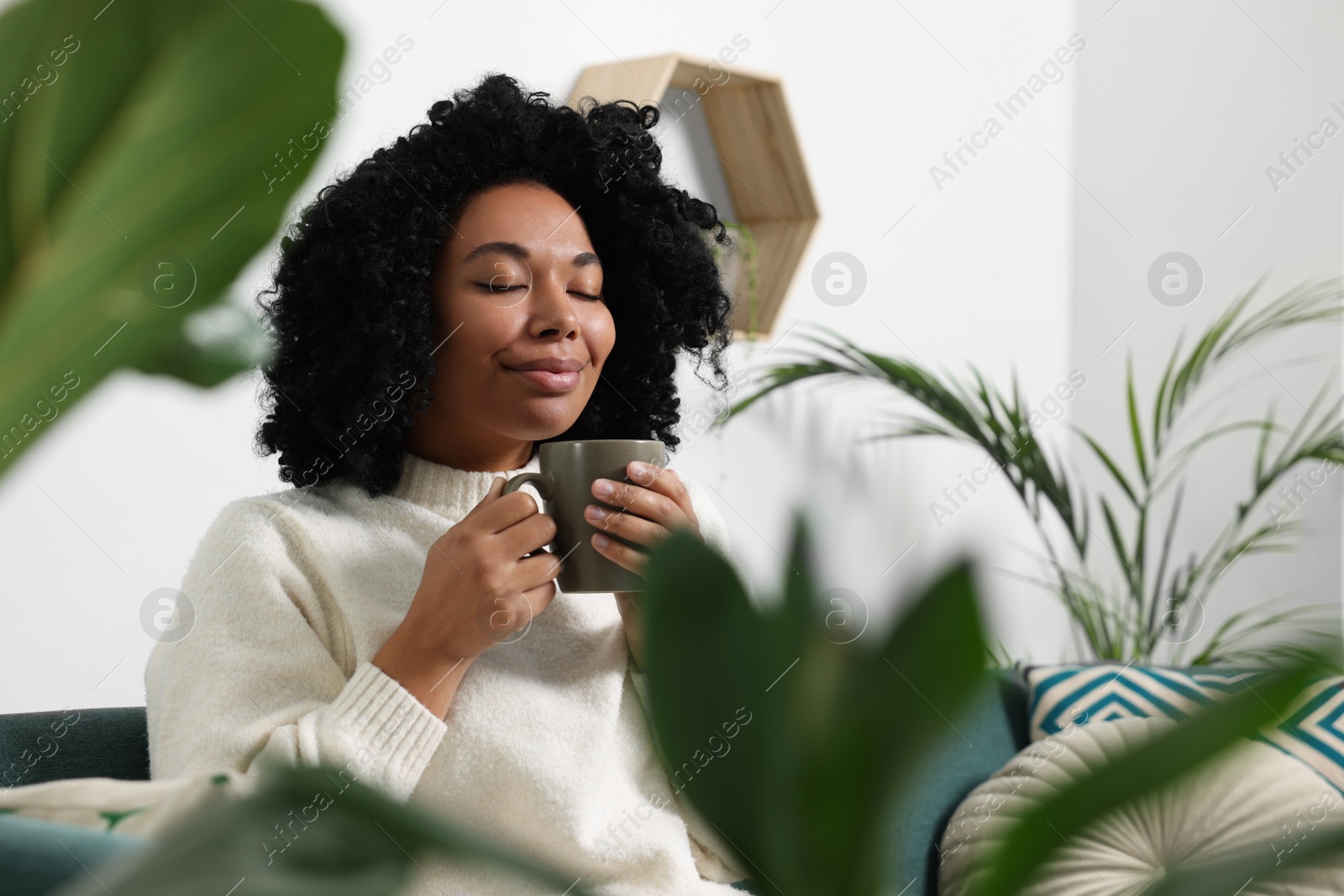 Photo of Relaxing atmosphere. Woman with cup of hot drink near beautiful houseplants indoors