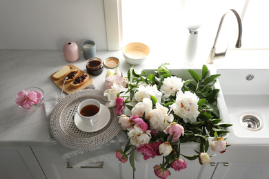 Photo of Beautiful peonies and breakfast on kitchen counter, above view