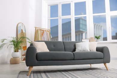 Photo of Stylish living room interior with comfortable grey sofa and clothing rack