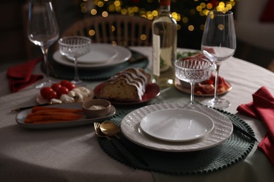 Photo of Christmas table setting with bottle of wine, appetizers and dishware