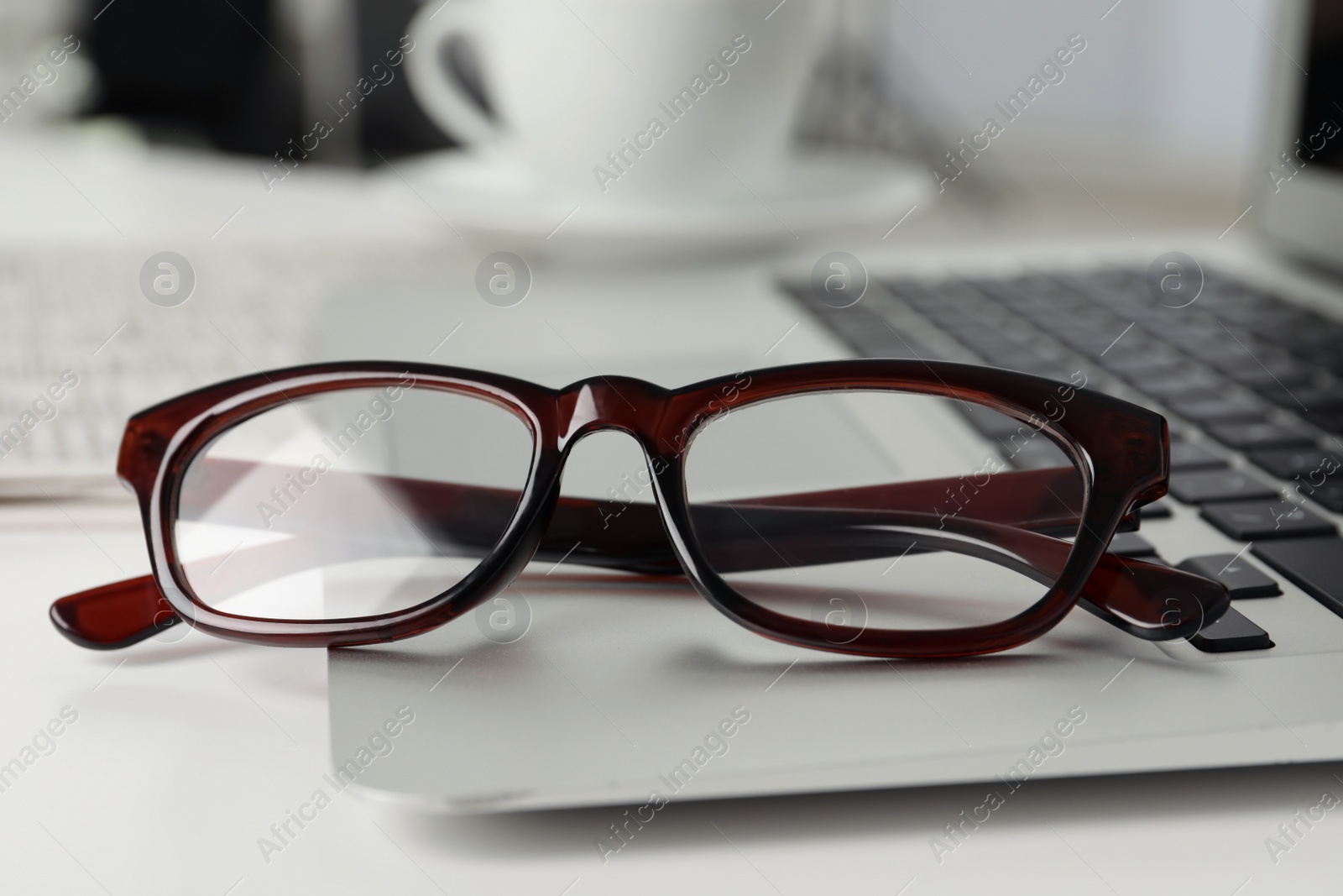 Photo of Modern laptop and glasses on white table, closeup