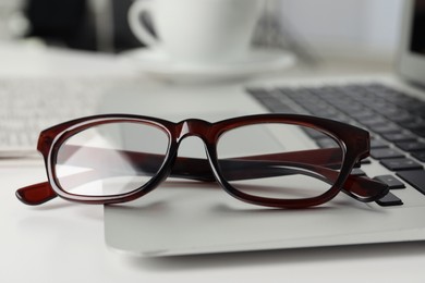 Modern laptop and glasses on white table, closeup