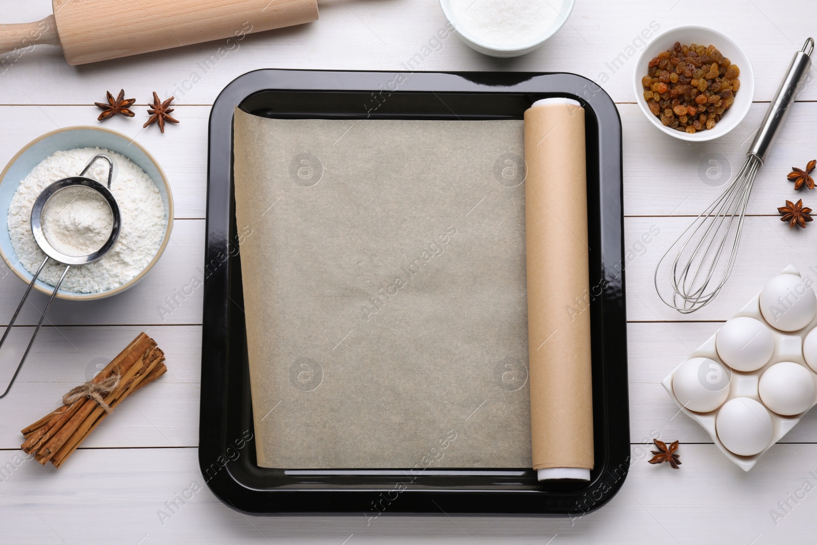 Photo of Baking pan with parchment paper, different ingredients and kitchen tools on white wooden table, flat lay