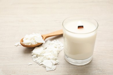 Photo of Burning soy candle, wax flakes and spoon on wooden table