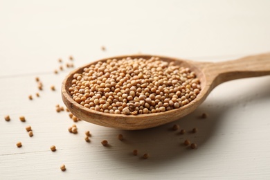 Photo of Mustard seeds with wooden spoon on white table, closeup