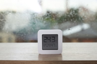 Photo of Digital hygrometer with thermometer near window on rainy day