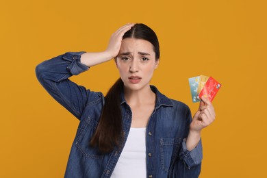 Photo of Worried woman with credit cards on orange background. Debt problem