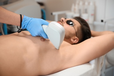 Photo of Young man undergoing laser epilation procedure in beauty salon