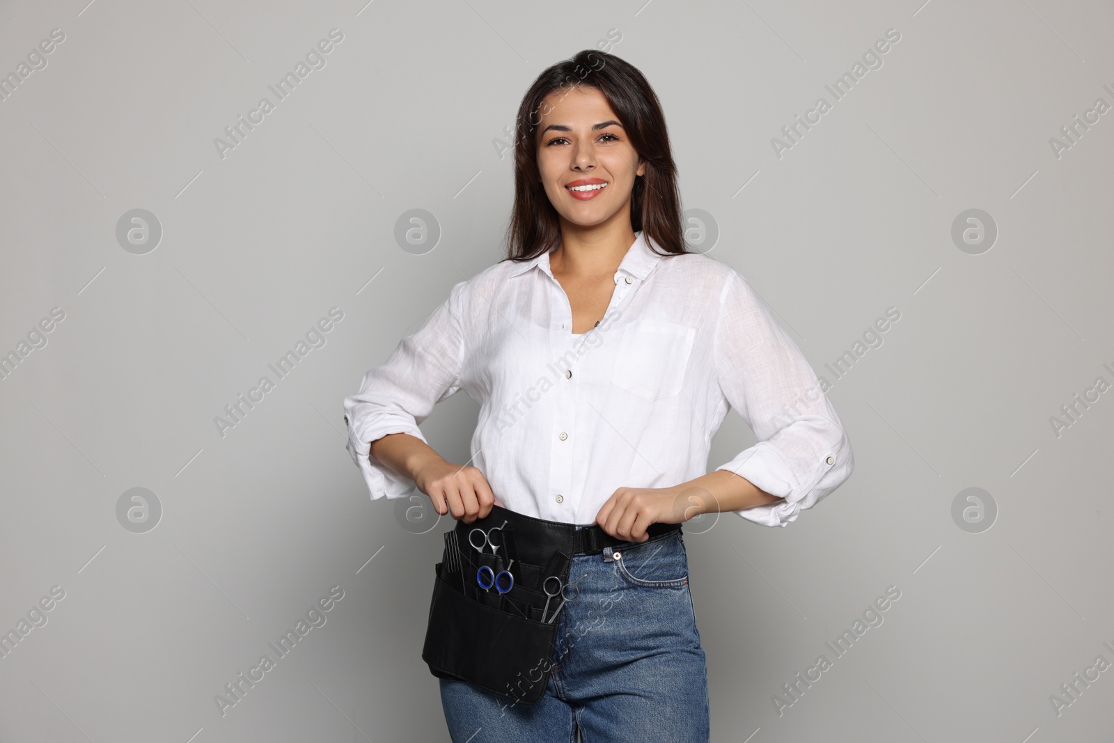 Photo of Portrait of happy hairdresser with professional tools on light grey background