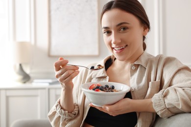 Photo of Woman eating tasty granola with fresh berries and yogurt at home