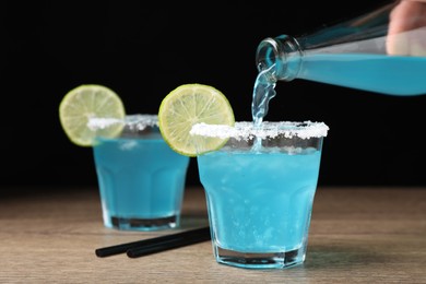 Photo of Bartender making cocktail with light blue drink at wooden table, closeup