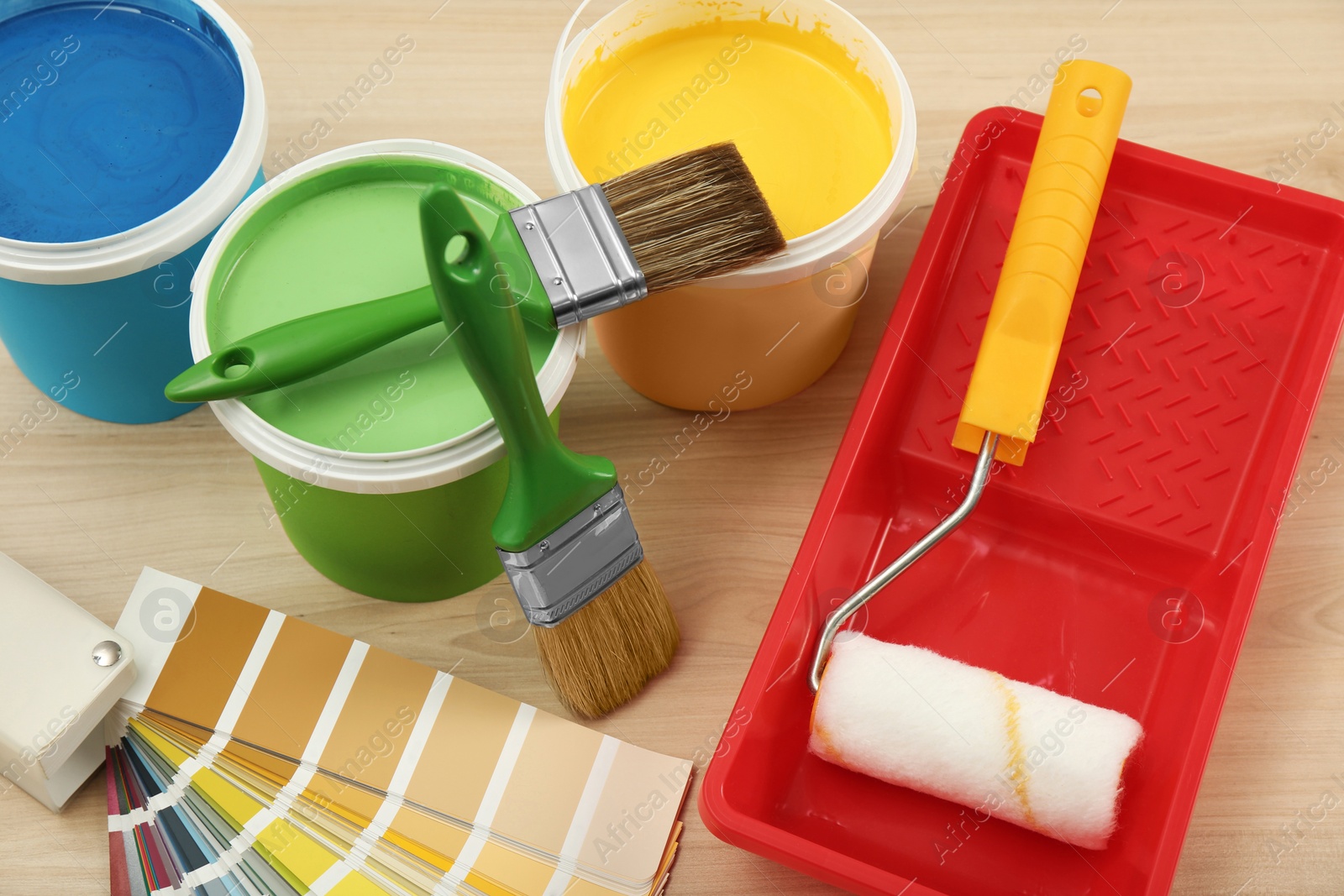 Photo of Buckets of paints, palette and decorator's tools on light wooden background, above view