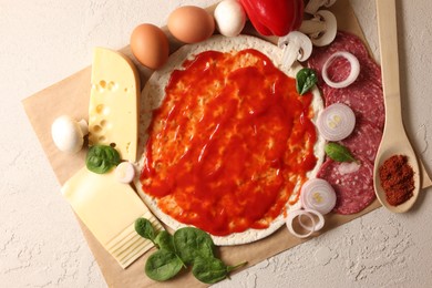 Pizza base smeared with tomato sauce and products on light textured table, top view