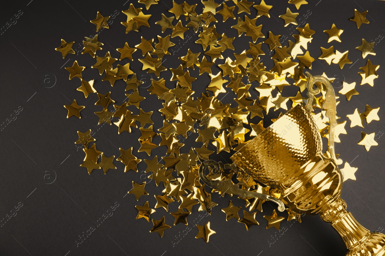 Photo of Gold trophy cup and confetti on black background, flat lay. Space for text