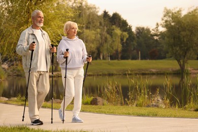 Senior man and woman performing Nordic walking outdoors, space for text