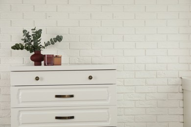 Photo of Modern chest of drawers with decor near white brick wall. Space for text