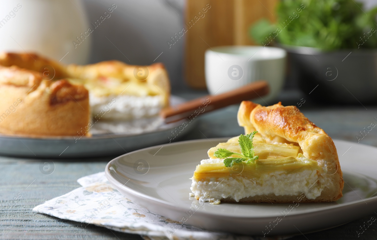 Photo of Piece of freshly baked rhubarb pie with cream cheese and mint leaves on grey wooden table, closeup