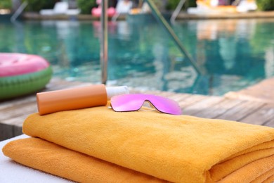 Beach towels, sunglasses and sunscreen on sun lounger near outdoor swimming pool, closeup. Luxury resort