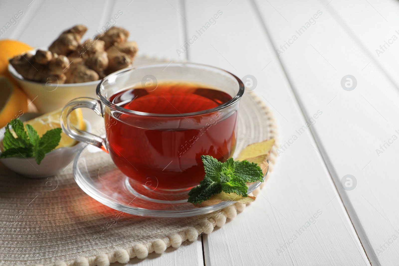 Photo of Cup of delicious ginger tea and ingredients on white wooden table