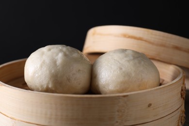 Photo of Delicious Chinese steamed buns in bamboo steamer against black background, closeup