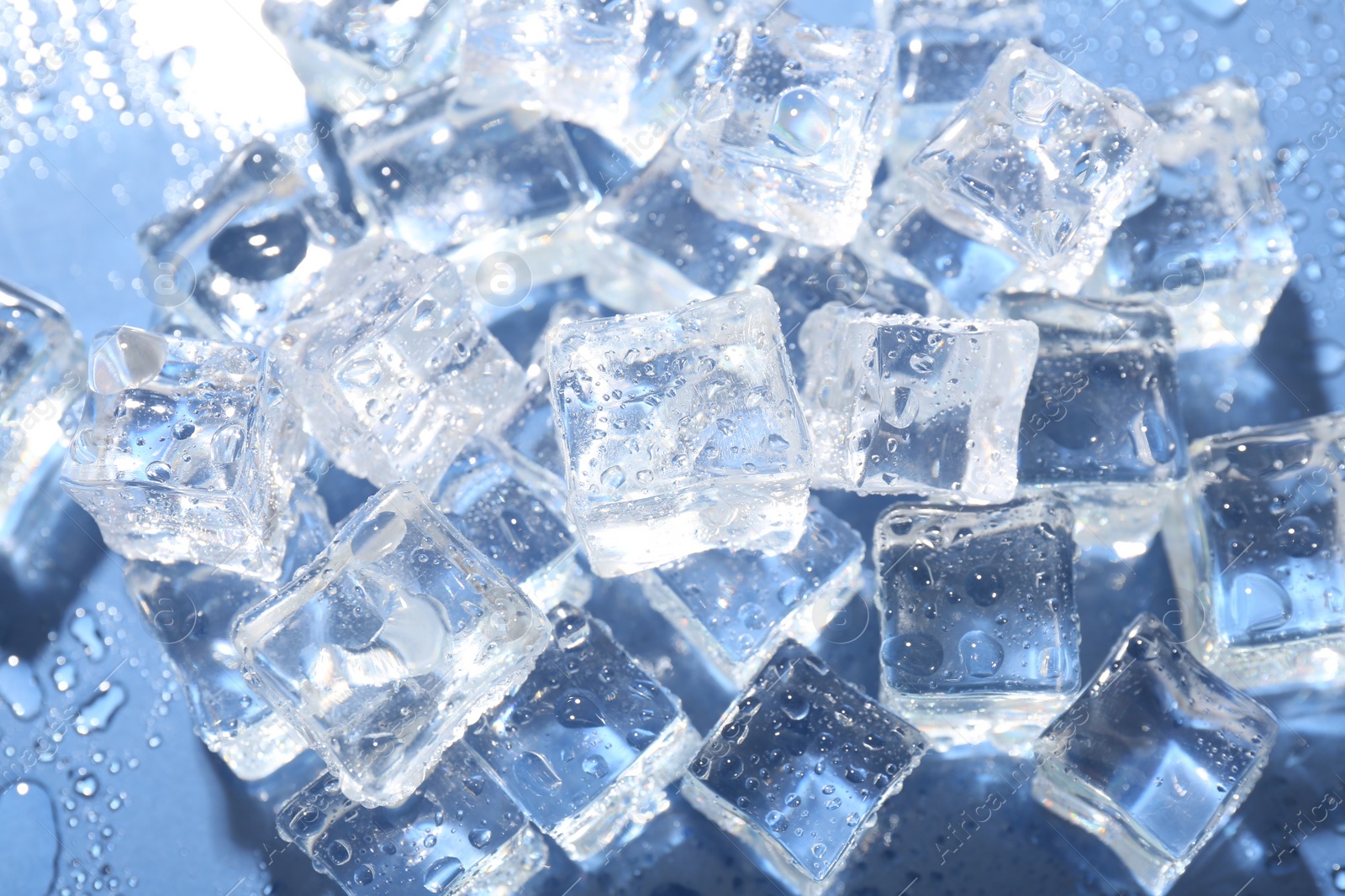 Photo of Melting ice cubes and water drops on blue background, above view