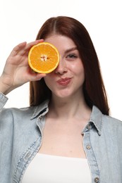 Beautiful woman covering eye with half of orange on white background