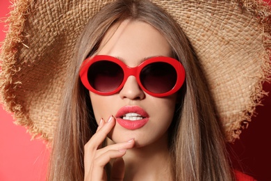 Photo of Young woman wearing stylish sunglasses and hat on red background