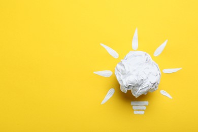 Photo of Composition with crumpled paper ball as lamp bulb on yellow background, top view and space for text. Idea concept