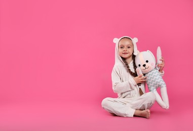 Photo of Cute girl wearing pajamas with toy on pink background. Space for text
