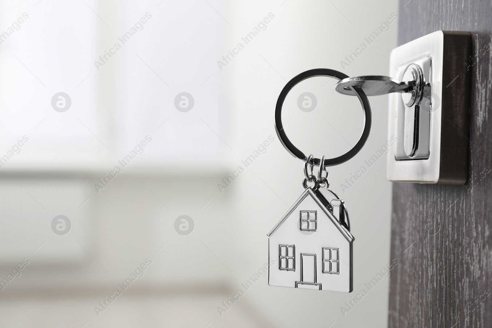 Photo of Mortgage and real estate. Open door with key and house shaped keychain against blurred background, space for text