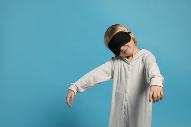 Photo of Boy in pajamas and sleep mask sleepwalking on light blue background, space for text