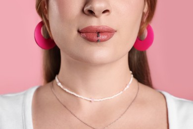 Young woman with lip piercing on pink background, closeup
