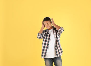 Photo of African-American teenage boy listening to music with headphones on color background