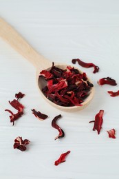 Photo of Hibiscus tea. Spoon with dried roselle calyces on white wooden table