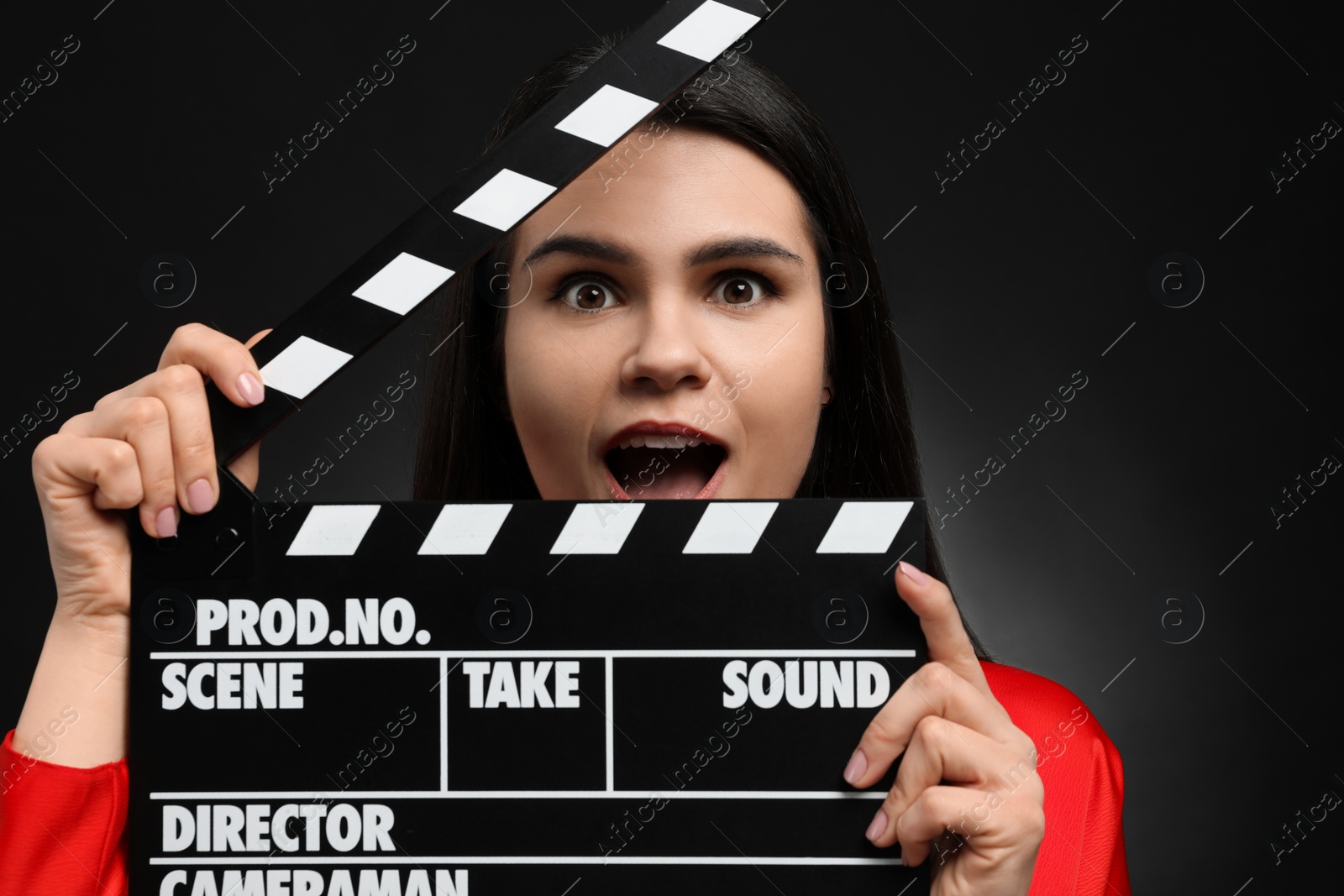 Photo of Emotional actress with clapperboard on black background. Film industry