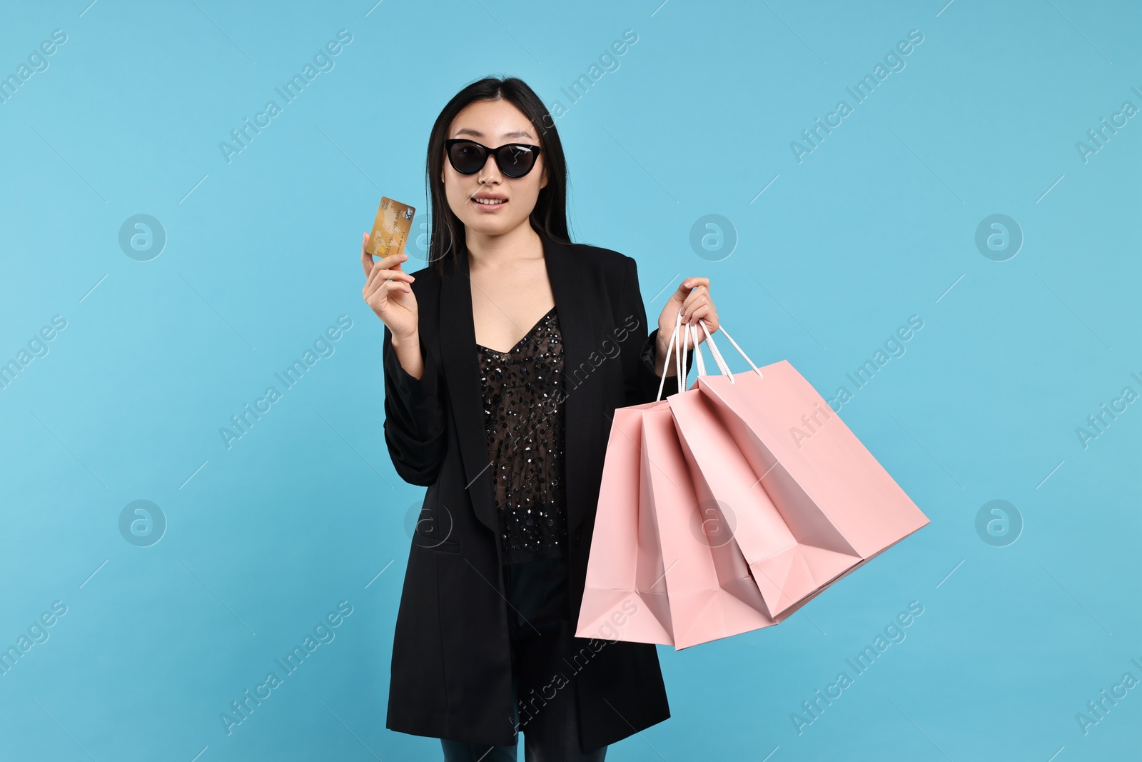Photo of Smiling woman with shopping bags and credit card on light blue background