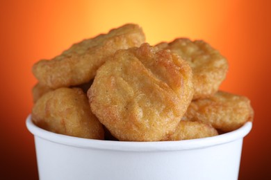 Bucket with delicious chicken nuggets on orange background, closeup