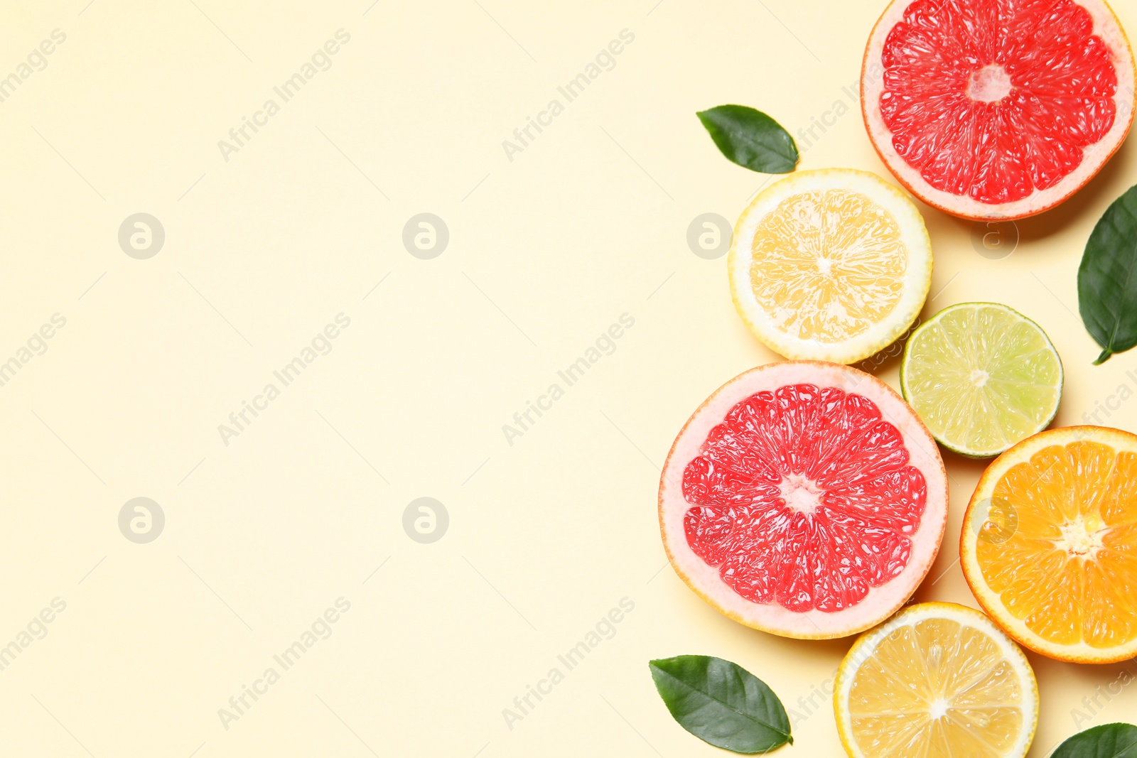 Photo of Different cut citrus fruits and leaves on beige table, flat lay. Space for text