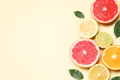 Photo of Different cut citrus fruits and leaves on beige table, flat lay. Space for text